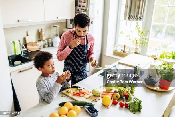 single dad snacking with his son while preparing lunch - man cooking at home stock pictures, royalty-free photos & images