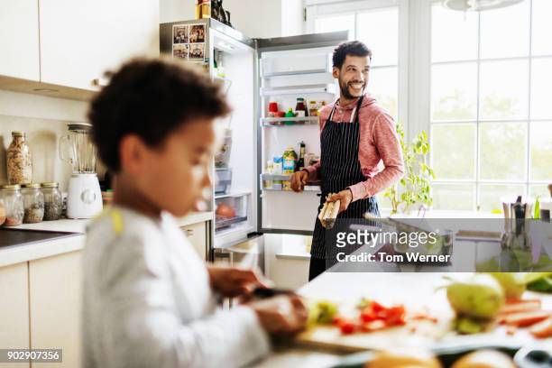 single dad smiling while he prepares lunch for son at home - refrigerator stock pictures, royalty-free photos & images