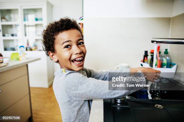 young boy grinning while washing hands in kitchen sink - boys with braces stock pictures, royalty-free photos & images