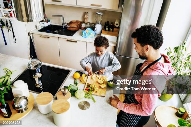 father and son in kitchen preparing salad together - generationen kochen stock-fotos und bilder
