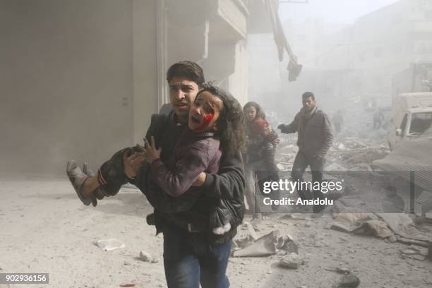 Syrian man carries a wounded girl after war crafts belonging to Assad Regime carried out airstrikes in the de-escalation zone of Hamouriyah, in...