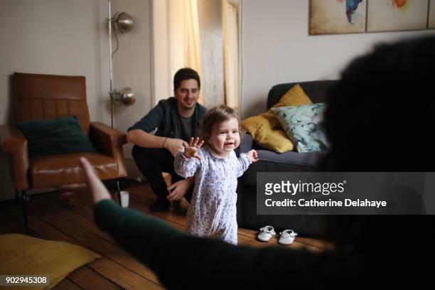 a 1 year old baby girl is taking her first steps at home - differential focus fotografías e imágenes de stock