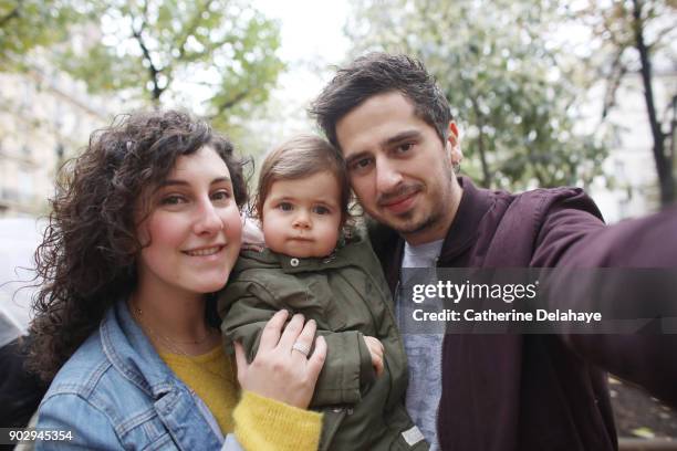 a 1 year old baby girl in the arms of her parents in the street - 25 year man ストックフォトと画像