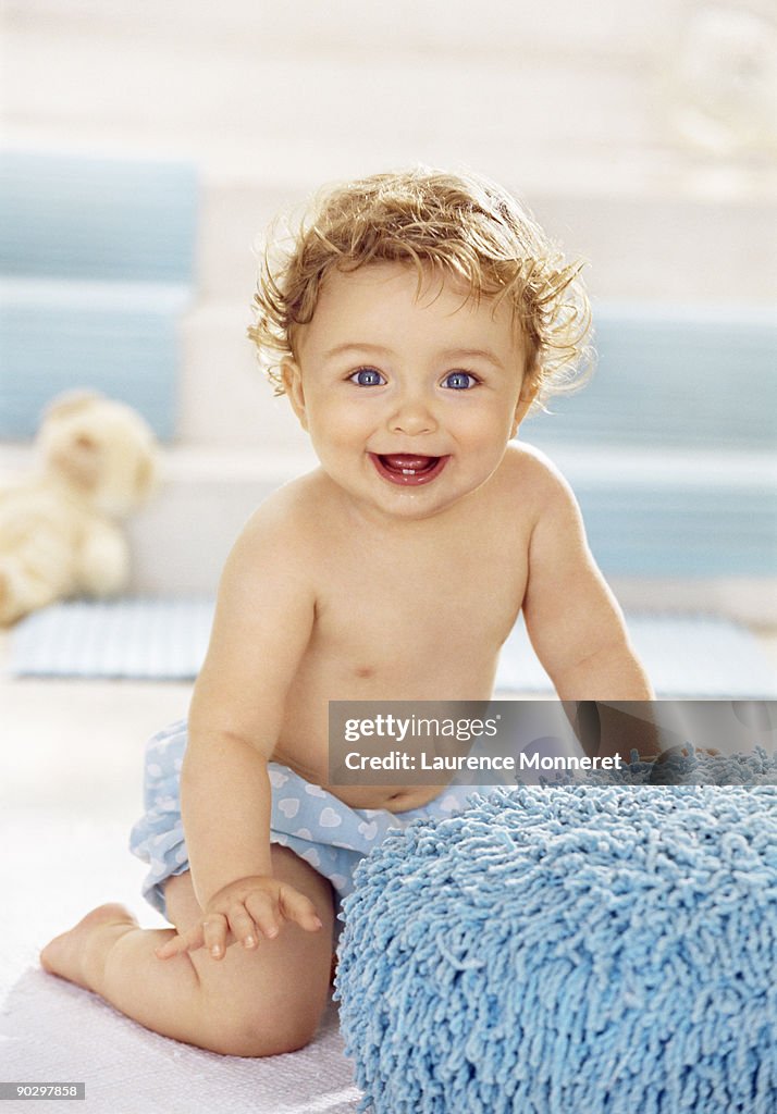 Smiling baby boy leaning on a blue footrest