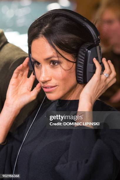 Britain's Prince Harry's fiancée US actress Meghan Markle listens to a broadcast through headphones during a visit to Reprezent 107.3FM community...