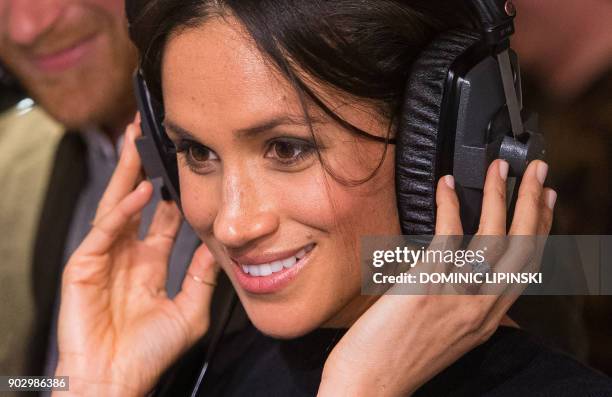 Britain's Prince Harry's fiancée US actress Meghan Markle listens to a broadcast through headphones during a visit to Reprezent 107.3FM community...