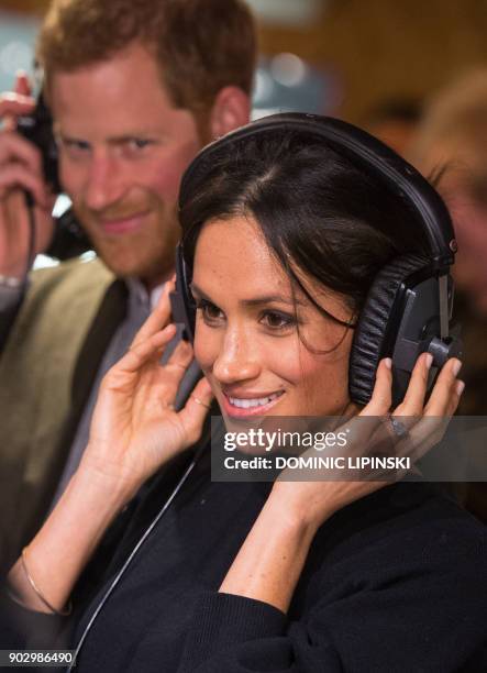 Britain's Prince Harry and his fiancée US actress Meghan Markle listen to a broadcast through headphones during a visit to Reprezent 107.3FM...