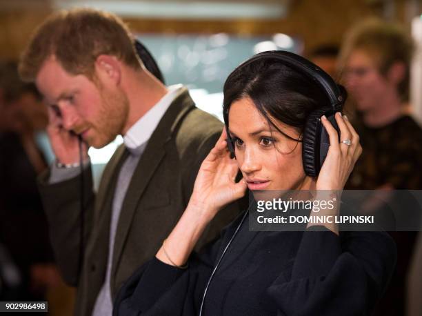Britain's Prince Harry and his fiancée US actress Meghan Markle listen to a broadcast through headphones during a visit to Reprezent 107.3FM...
