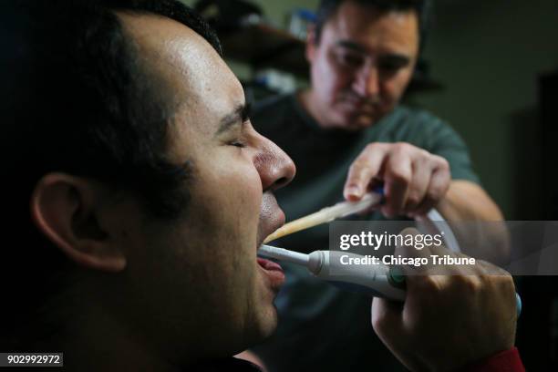 Jose Rodriguez Jr. Brushes his teeth while his dad, Jose Rodriguez Sr., suctions him at their home on Wednesday, Dec. 13, 2017 in Aurora, Ill. In...