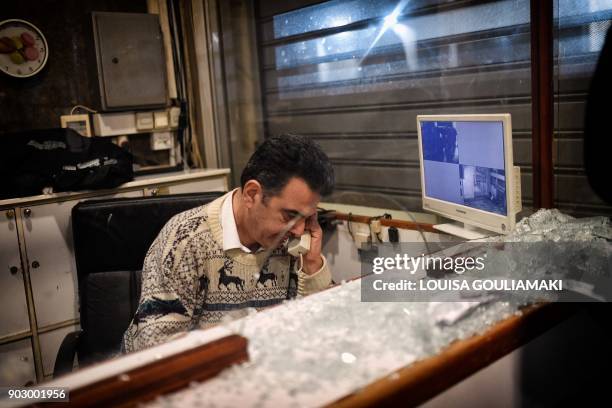 Security employee of the Labour Ministry makes a phone call by a shattered glass after Communist-affiliated PAME workers unionists stormed the Labour...