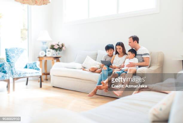 family using digital tablet in living room - family on couch stock pictures, royalty-free photos & images