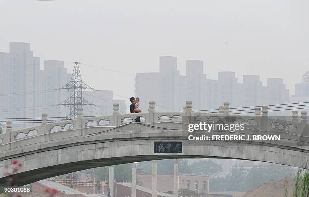 Man carries a child across a footbridge over a canal on a hazy day in Beijing on August 18, 2009. China could see its greenhouse gas emissions peak...