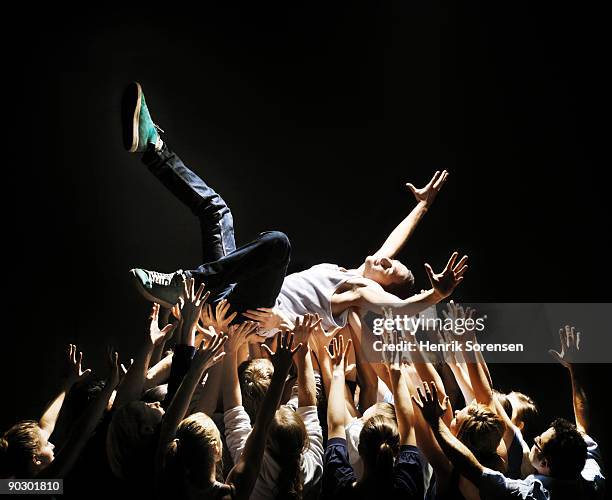 young man beeing carried by group of people - concierto de música pop rock fotografías e imágenes de stock