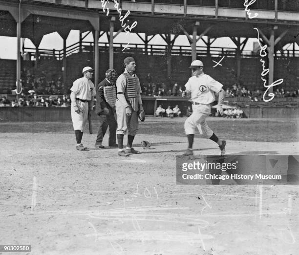 Watched by an unidentified teammate , American baseball player Frank Chance of the Chicago Cubs crosses home plate as Canadian catcher George Gibson...