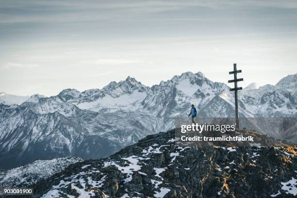 person next to a summit cross with massive mountains in the background - kuehtai foto e immagini stock