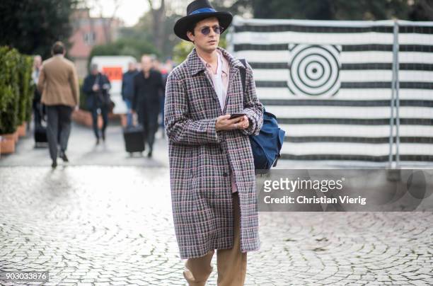 Alessandro Enriquez wearing hat, checked coat, beige track suit is seen during the 93. Pitti Immagine Uomo at Fortezza Da Basso on January 9, 2018 in...