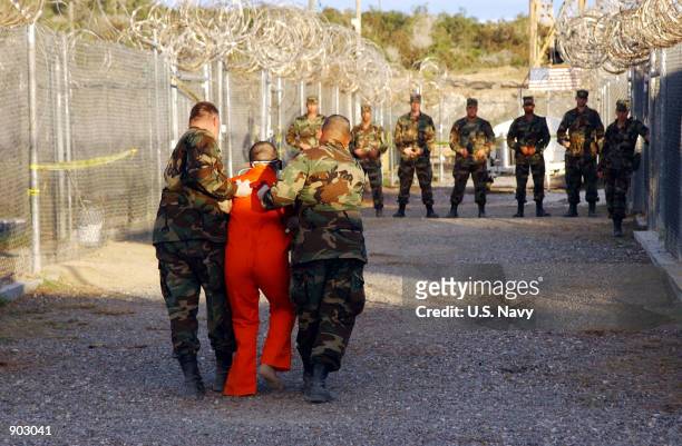 Army Military Police escort a detainee to his cell January 11, 2001 in Camp X-Ray at Naval Base Guantanamo Bay, Cuba, during in-processing to the...