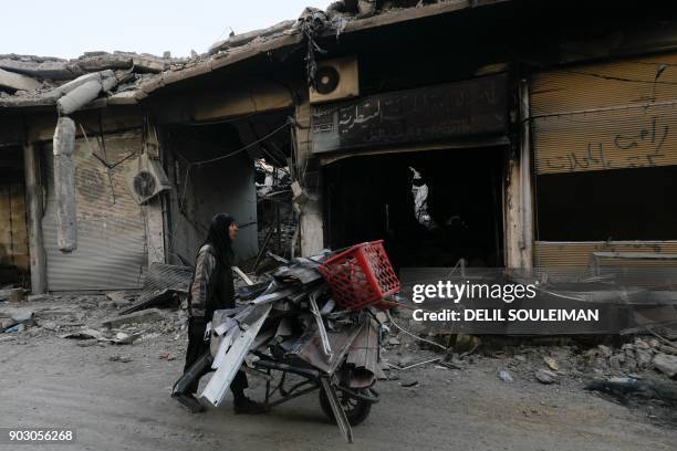 Woman pulls a cart loaded with pieces of metal in Syria's devastated city of Raqa on January 9, 2018.