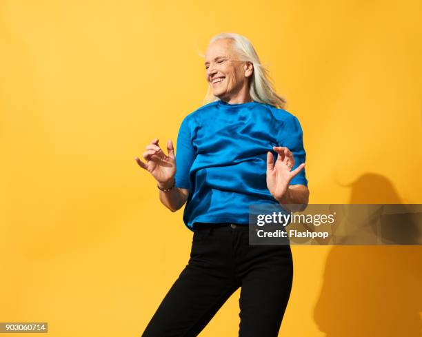 portrait of mature woman dancing, smiling and having fun - sfondo giallo foto e immagini stock