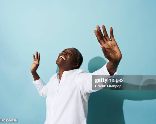 portrait of mature woman dancing, smiling and having fun - portrait blue background stock-fotos und bilder