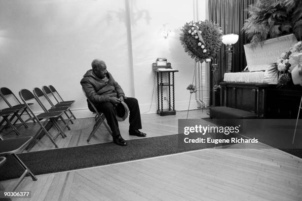 An elderly man sits in front of his grandson's open coffin at a funeral home, Brooklyn, New York, New York, April 1988. His grandson was fifteen when...