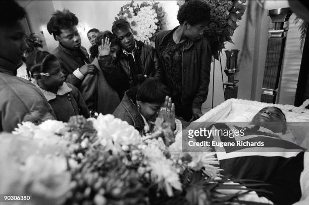 View of mourners gathered around an open coffin at a funeral home, Brooklyn, New York, New York, April 1988. They were paying their respects to a...