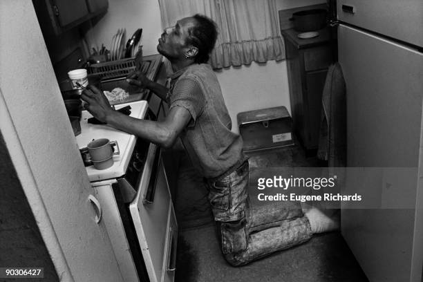 View of a man as he smokes a crack pipe, kneeling in front of a stove in a kitchen in the Red Hook Houses, Brooklyn, New York, 1988. The photo was...