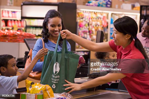 mixed race woman using reusable bag in grocery store - wiederverwendbare tasche stock-fotos und bilder