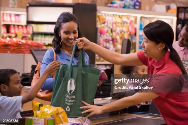 mixed race woman using reusable bag in grocery store - shopping bag stock photos et images de collection