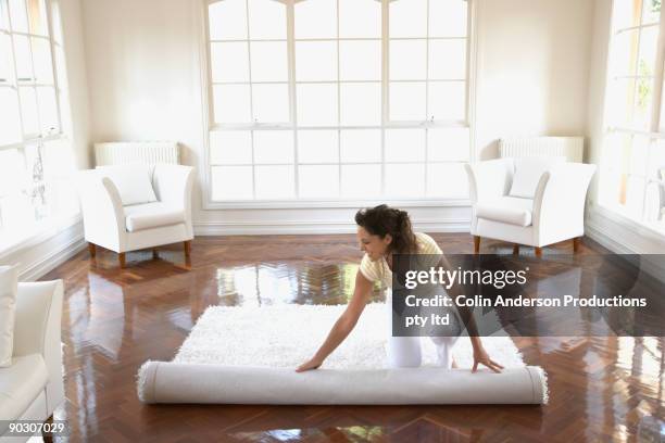 hispanic woman unrolling rug in new home - new from rolls press stock-fotos und bilder