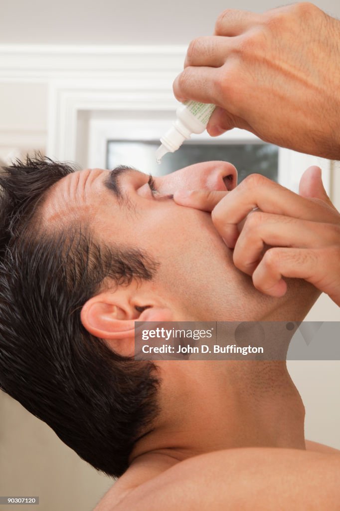 Hispanic man using eye drops