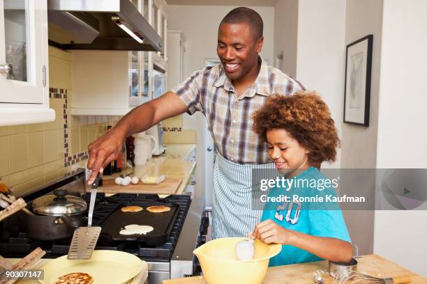 african father and son making pancakes - gusseiserne pfanne stock-fotos und bilder