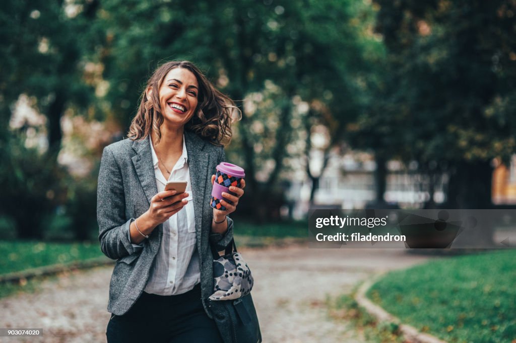 Woman texting and drinking coffee in the park