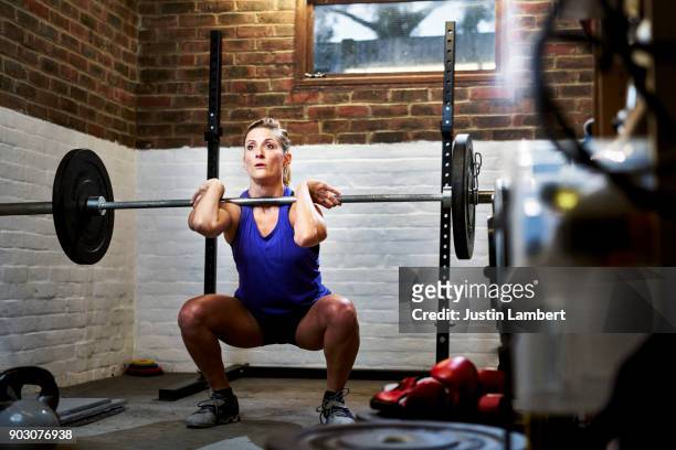 woman exercising in home gym in converted garage performing a squat or clean - weight training stock pictures, royalty-free photos & images