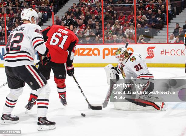 Anton Forsberg of the Chicago Blackhawks makes a save against Mark Stone of the Ottawa Senators as Gustav Forsling of the Chicago Blackhawks looks on...