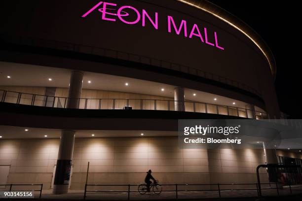 Woman rides a bicycle in front of Aeon shopping mall, operated by Aeon Mall Co., a unit of Aeon Co., at night in Chiba, Chiba Prefecture, Japan, on...
