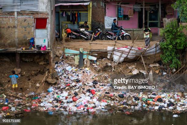 Children are seen beside a trash thrown into a riverbank at a slum in Jakarta on January 10, 2018.
