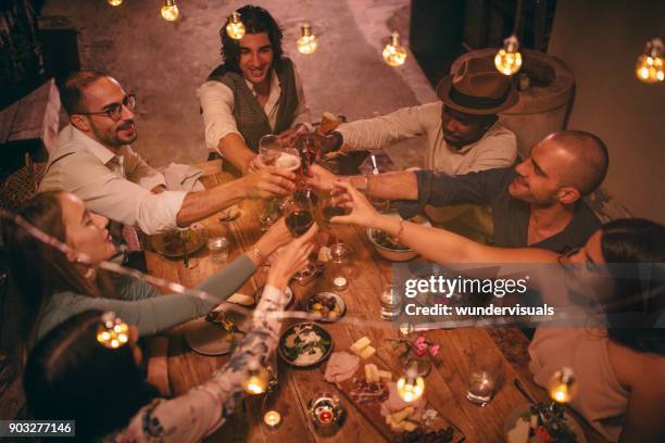 young multi-ethnic friends celebrating and toasting at rustic dinner party - italy beer stock pictures, royalty-free photos & images