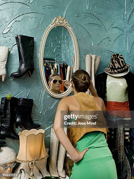 woman looking in mirror in second-hand store - woman mirror dress stock-fotos und bilder