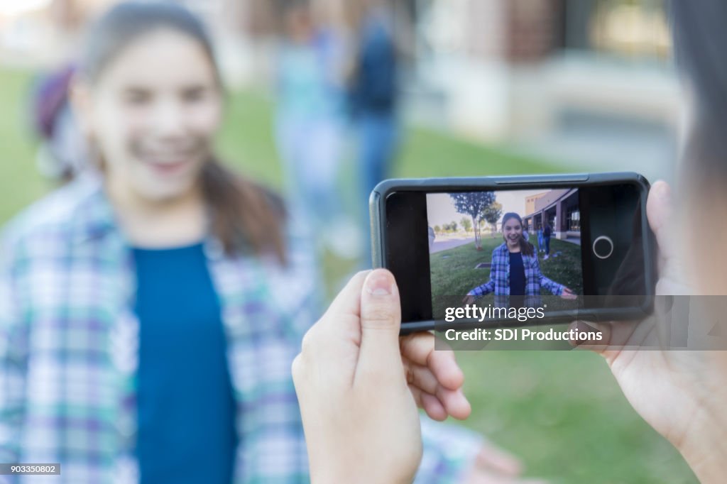 Smart phone taking photo of teen girl outside high school