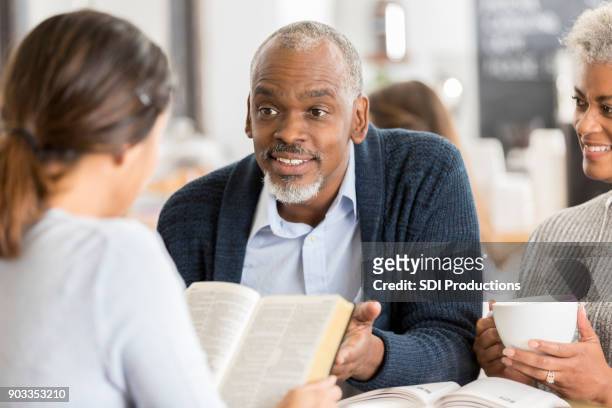 a senior couple explain bible passage to young woman - preacher stock pictures, royalty-free photos & images