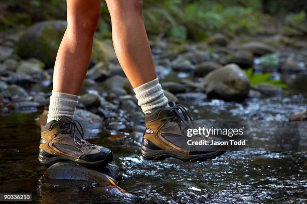 woman crossing stream wearing hiking boots - wanderschuhe stock-fotos und bilder