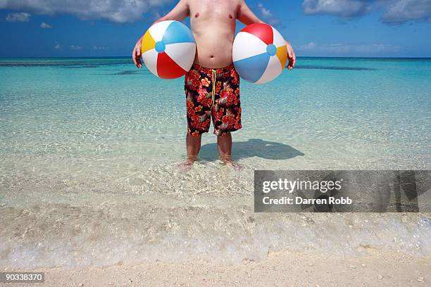 man holding beach balls on tropical beach - swimming shorts stock pictures, royalty-free photos & images