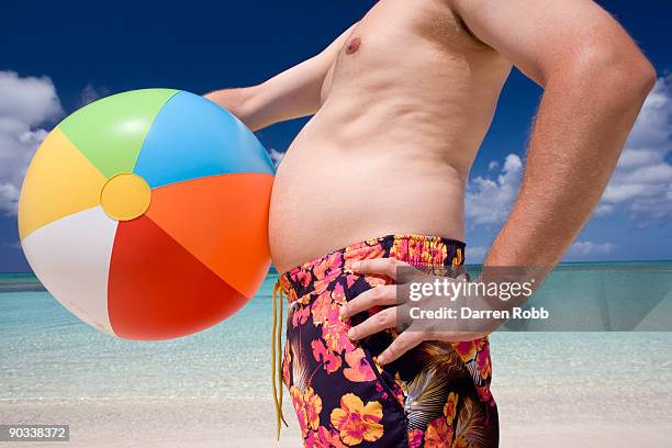 man holding a beach ball against stomach on beach - bierbauch stock-fotos und bilder
