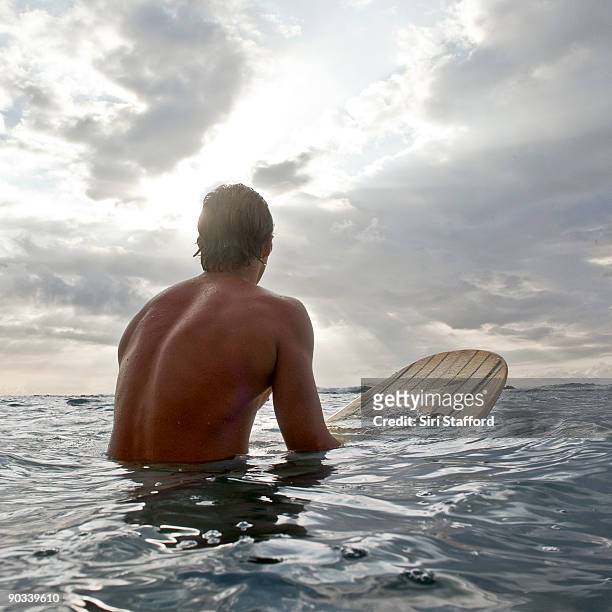 young man on surfboard in water looking out - siri stafford stock pictures, royalty-free photos & images