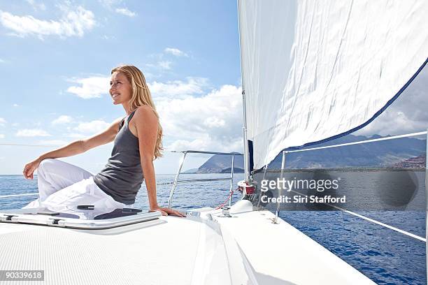 young woman sitting on bow of sailboat, smiling - siri stafford stock pictures, royalty-free photos & images