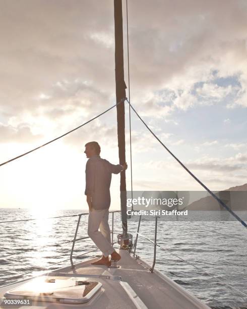 man standing on bow of sailboat at sunset - siri stafford stock pictures, royalty-free photos & images