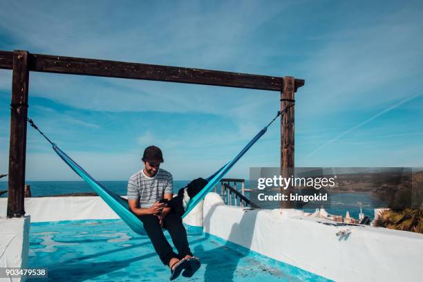 man sitting in hammock and looking at his smartphone - man sleeping with cap stock pictures, royalty-free photos & images