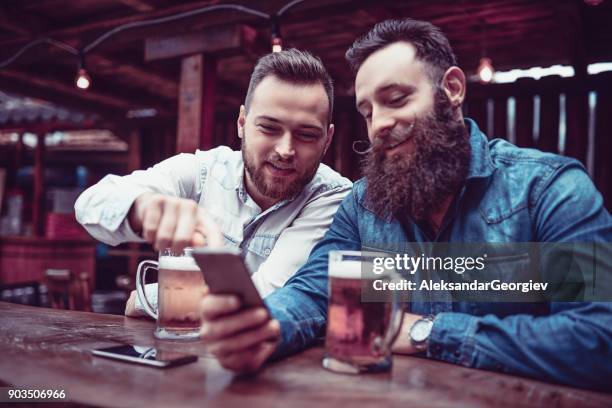 dos amigos hipster barbudo sonriente bebiendo cerveza y usar teléfono móvil - like a boss film fotografías e imágenes de stock