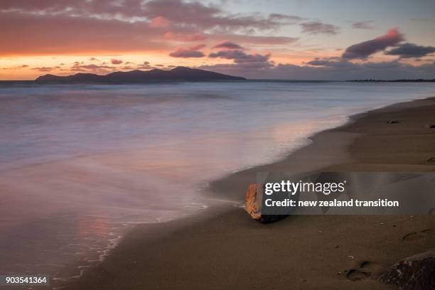 pink sunset sky over sandy beach and kapiti island with long exposure of ocean waves - kapiti coast stock pictures, royalty-free photos & images